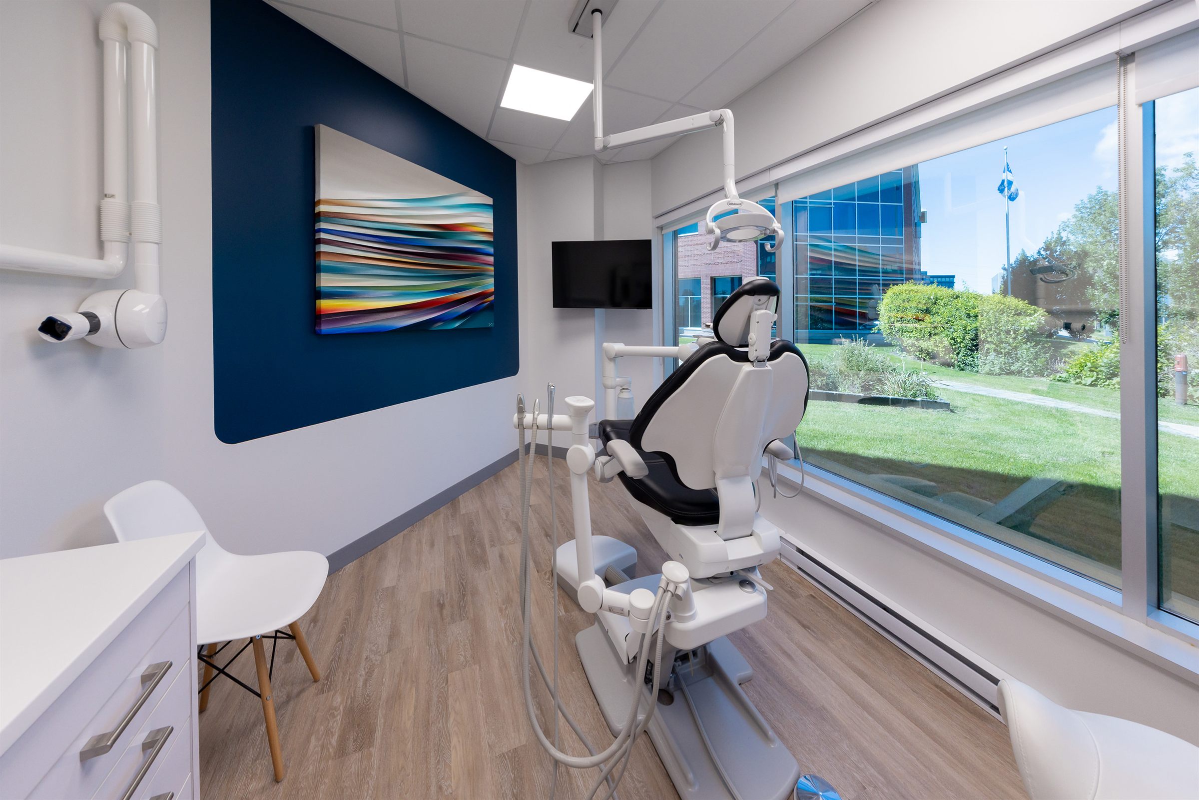 Salle de traitement au mur bleu marine et fauteuil dentaire face à la fenêtre, clinique à Lebourgneuf, Québec